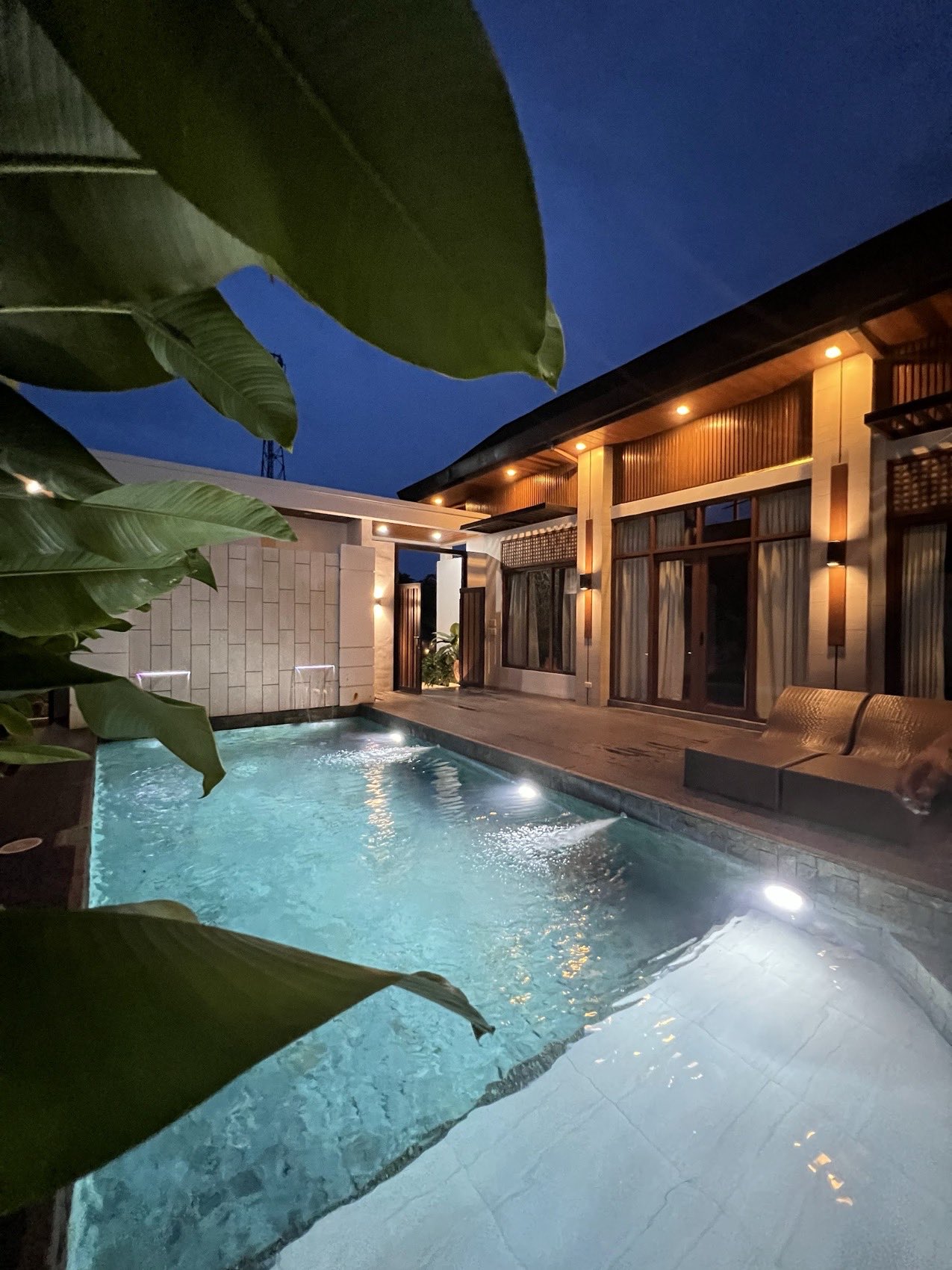 Casa Uno's lit pool and villa at blue hour, framed by banana leaves